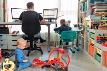 Stock photo of two children playing while adult works on computer